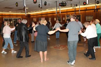 A circle of dancers hold hands as they step forward to the center of the circle.